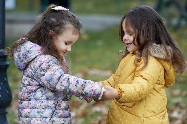 Two small girls hold hands while dancing.