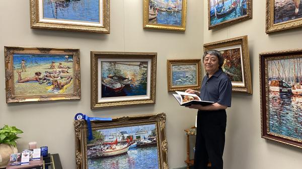 photograph of Yan Sun surrounded by colorful paintings